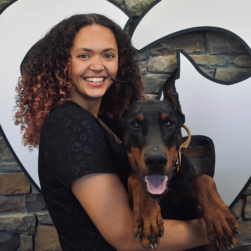 Female with dark curly hair holding a very large black and brown dog